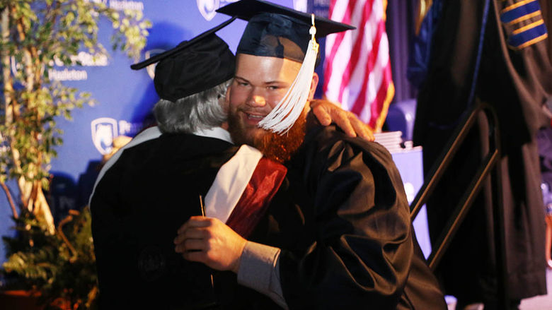 Graduate hugging professor during commencement ceremony. 