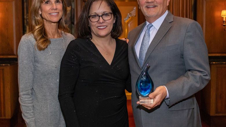 three people smiling at camera, one is holding a tear drop award 