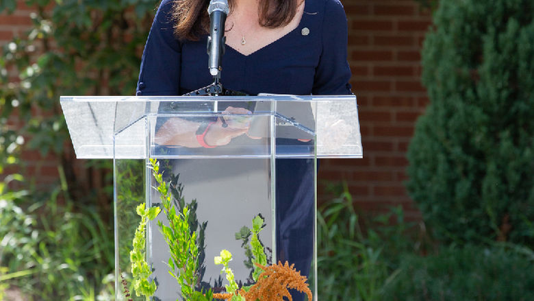 woman standing behind clear podium talking into microphone