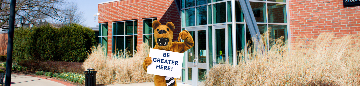 Lion standing in front of the SCC holding sign that reads BE Greater Here
