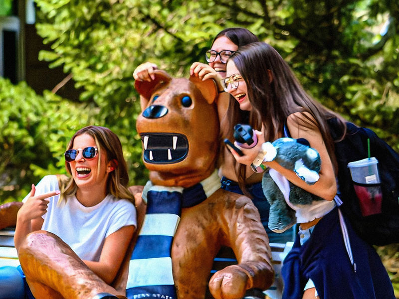 A group of female students share laughter and smiles as they pose for a photo with the iconic Nittany Lion mascot