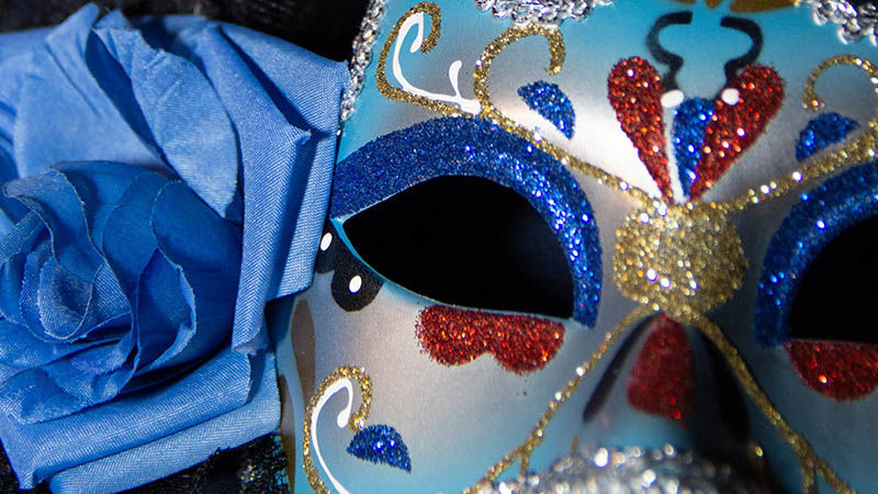 Masquerade mask sitting next to rose