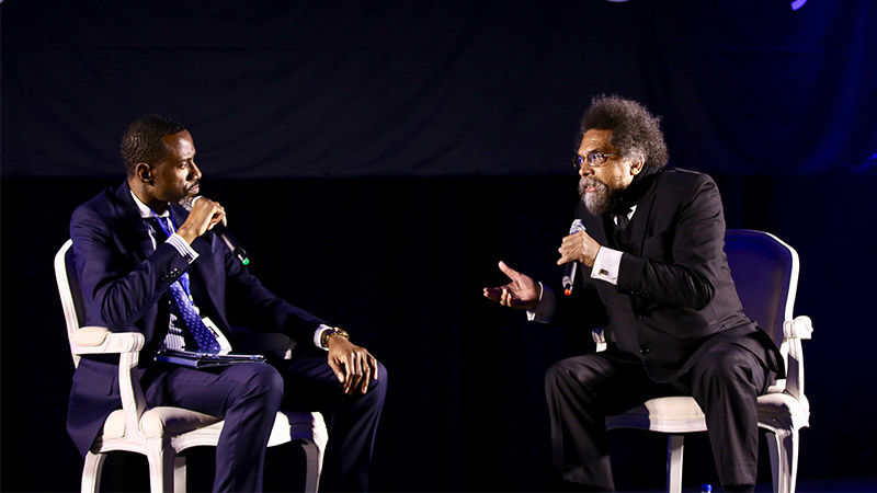 two men sitting on stage talking into microphone