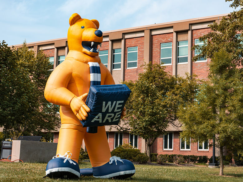 Inflatable, Tall, Nittany Lion holding a "We Are" sign,  situated on the Buck Lawn in front of the Frable Building