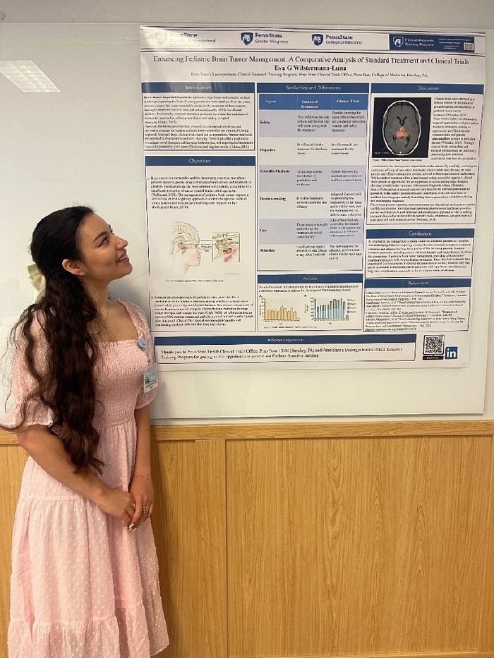 A woman stands to the left of a poster describing her experience in a clinical research internship program.