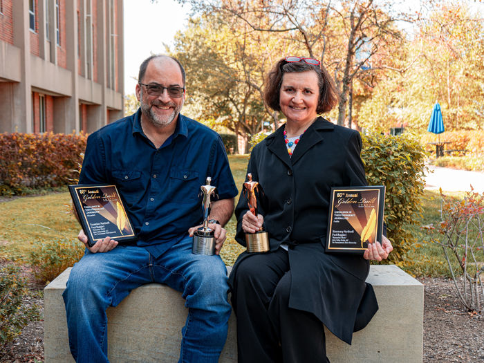 two people outside each holding a plaque and an award statute.  