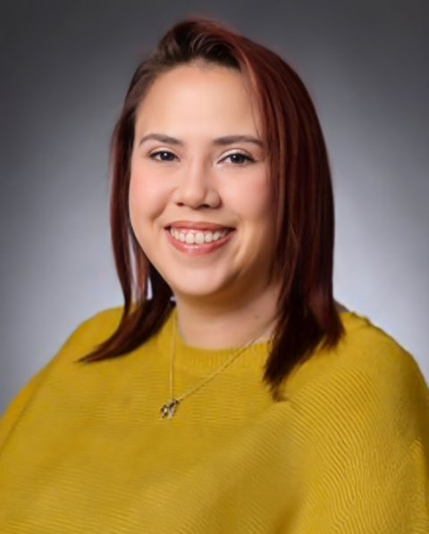 Photo of Upward Bound Assistant Director, West, Ashley Pesi, MSW, wearing a bright yellow sweater and smiling for her directory photo, taken in front of a grey back drop.