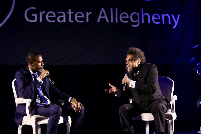 two men sitting on stage talking into microphone