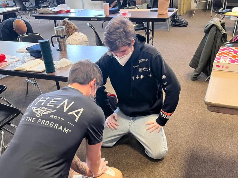 Two individuals practice chest compressions on a CPR dummy