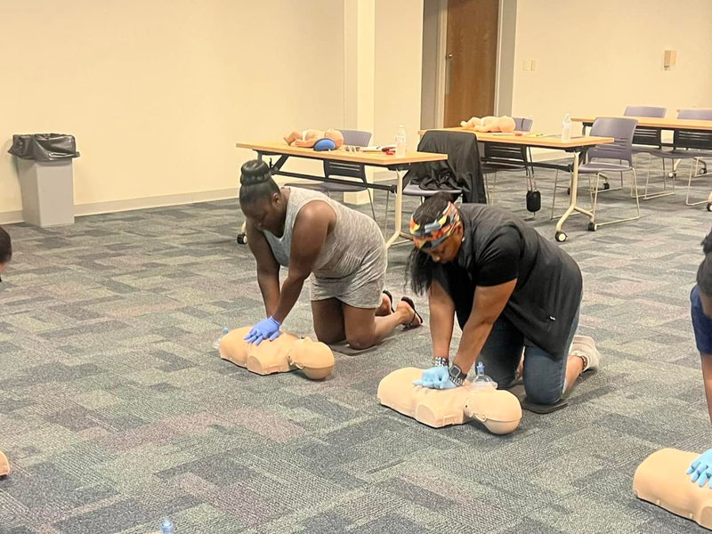 Two individuals perform chest compressions on CPR dummies