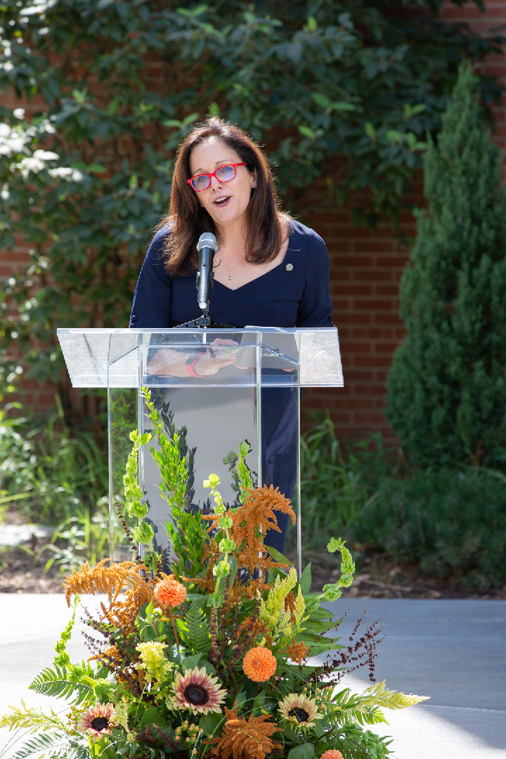 woman standing behind clear podium talking into microphone