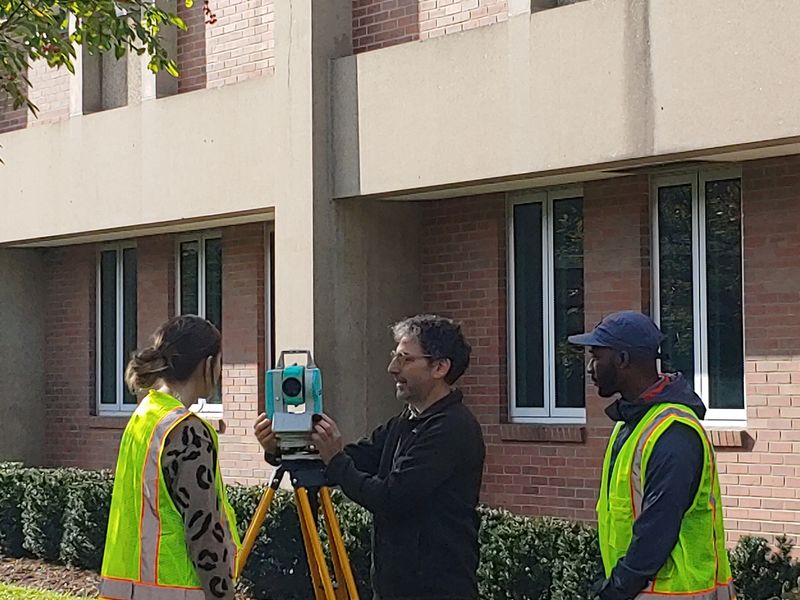 two students and a professor setting up a surveying camera in front of building