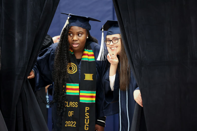 Administration of Justice (B.A.) Degree Candidate Sharon Ande and Criminal Justice (B.S.) Degree Candidate Samantha Penascino peak through the curtains in anticipation for the Fall 2022 Commencement Ceremony to begin.