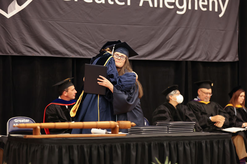 Student Marshal for Criminal Justice (B.S.), Samantha Penascino, receiving a hug and her diploma from Program Marshal for Administration of Justice and Criminal Justice, Dr. Kate McLean.