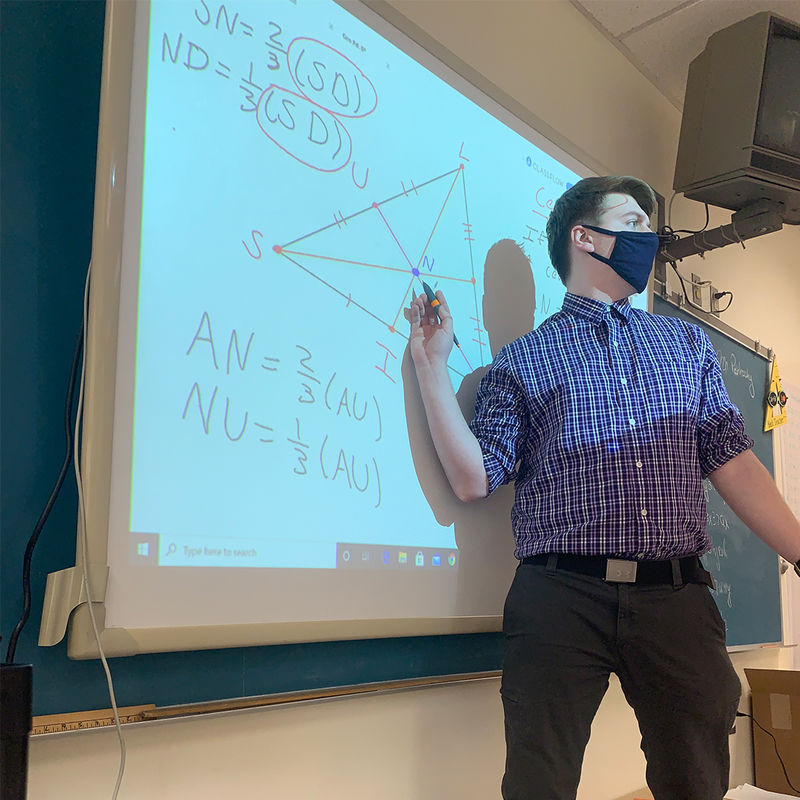 Student Teacher pointing at math problem on a projector while talking to class. 