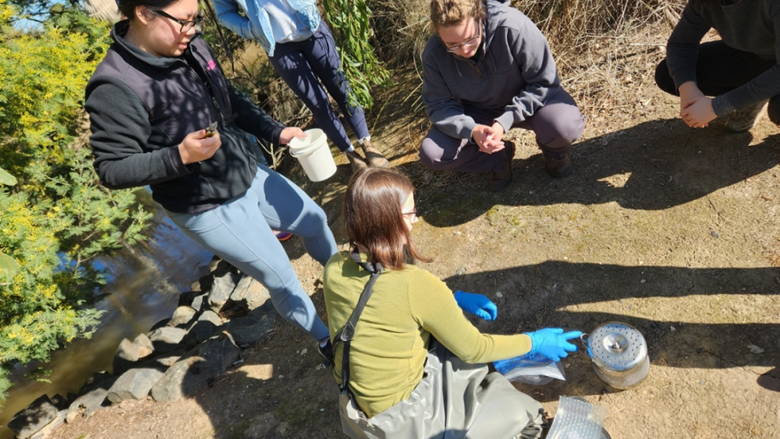 Students gathered around a water sampling device that is on the ground outside