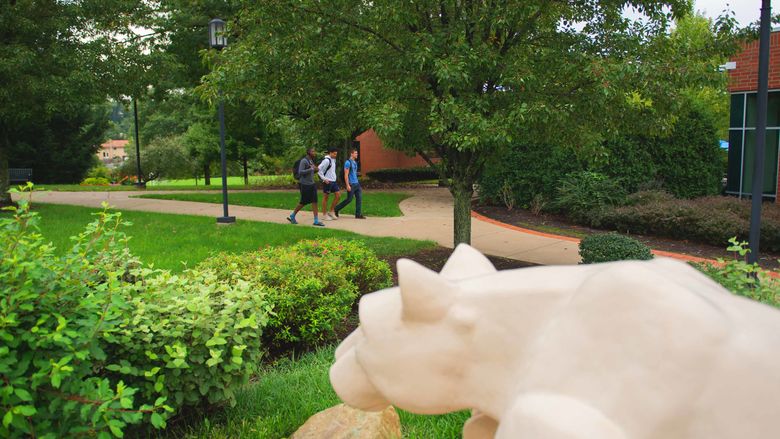 Two students walking in the background of the Nittany Lion shrine.
