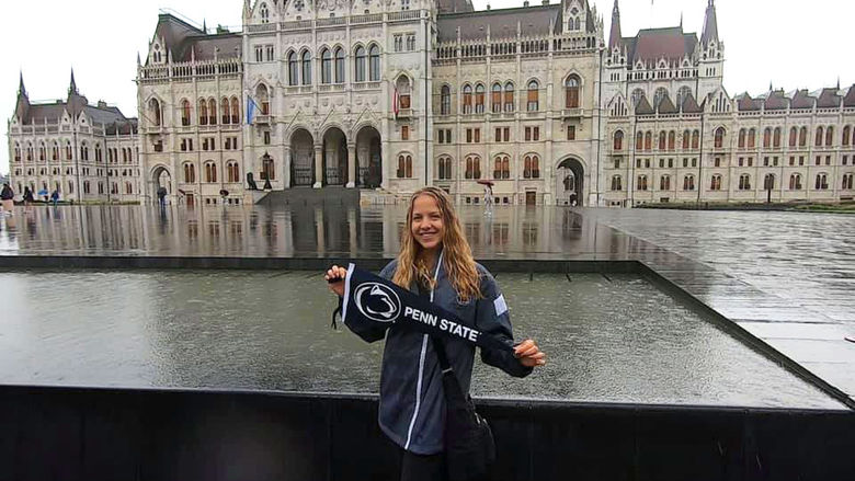 Student holding Penn State Flag in front of water feature