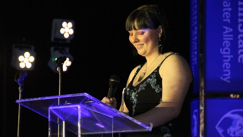 student at podium holding microphone smiling