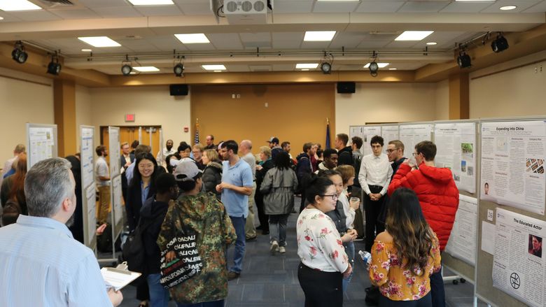 a big room with research poster on pin boards and a lot of people reviewing the research.