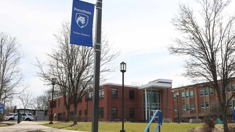 A light post with a banner on it that reads Penn State Greater Allegheny. It is positioned in front of a brick building. 
