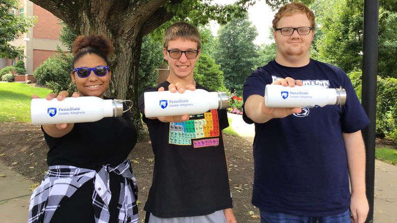 Three students holding white water bottles displaying Penn State Greater Allegheny's Logo 