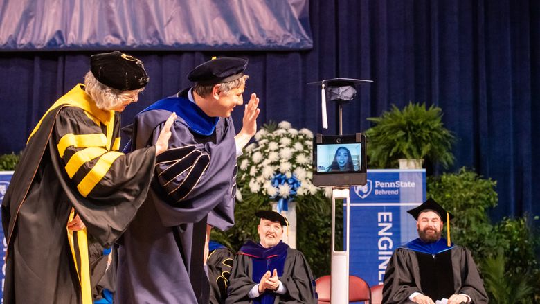 Two Penn State Behrend faculty members wave to a student whose face is on the monitor of a robot.