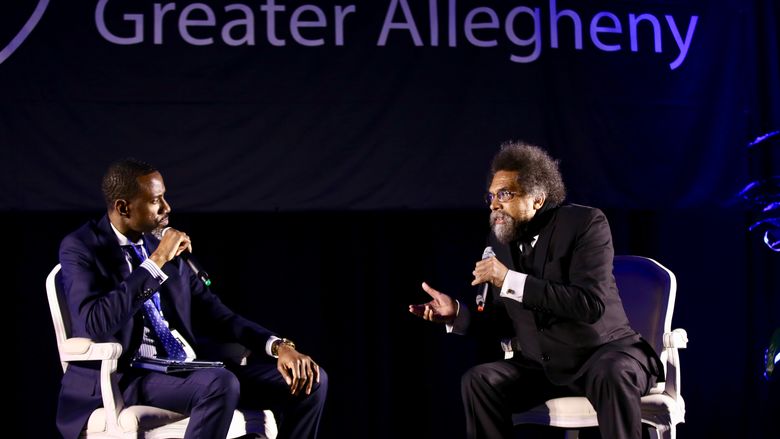 two men sitting on stage talking into microphone