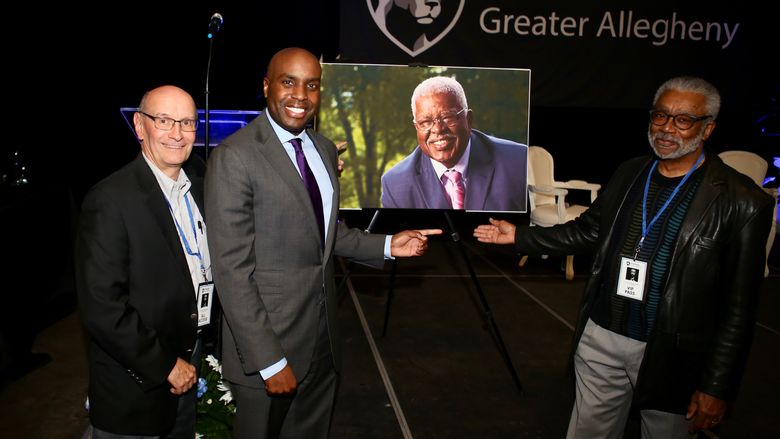 three men standing next to a portrait of another man. 