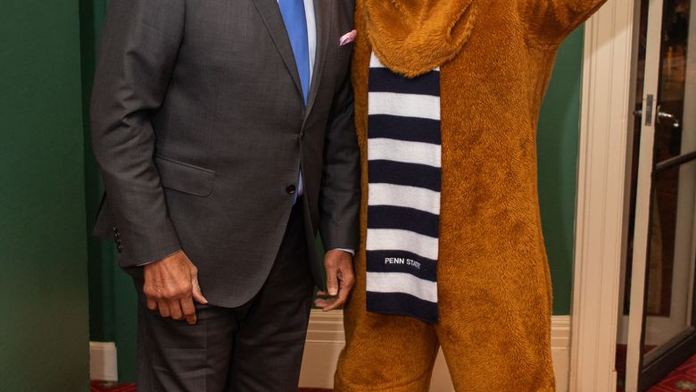 man smiling next to lion mascot who has index finger up forming a 1 
