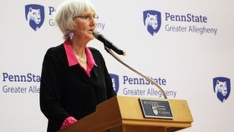 Woman speaking into a microphone that is attached to a wooden podium.