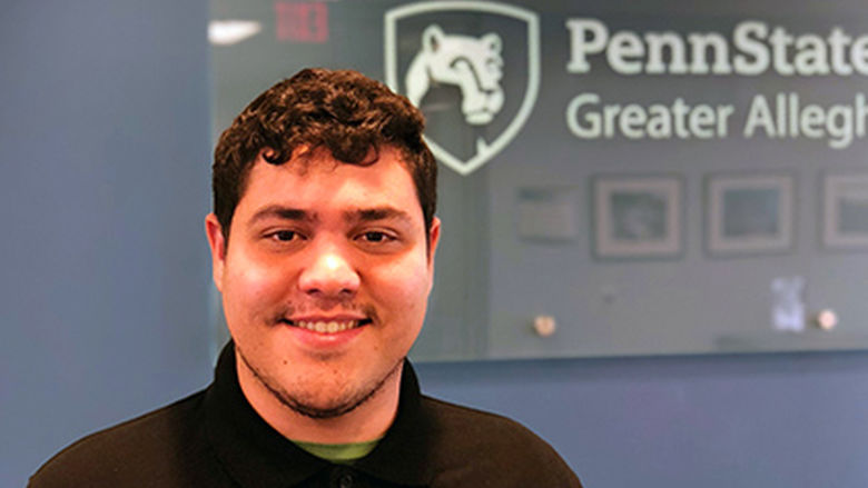 Student Derrick Ferrer Standing in front of Penn State Greater Allegheny Logo
