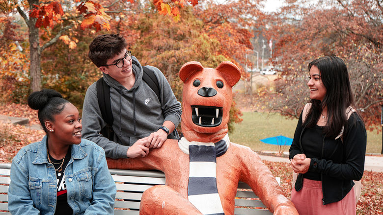 a group of students gather around the nittany lion bench for a photo