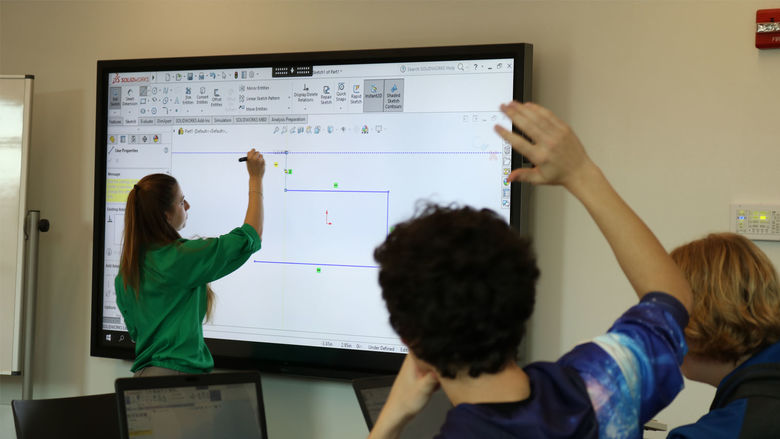 Student raising hand while professor draws on large screen televisione