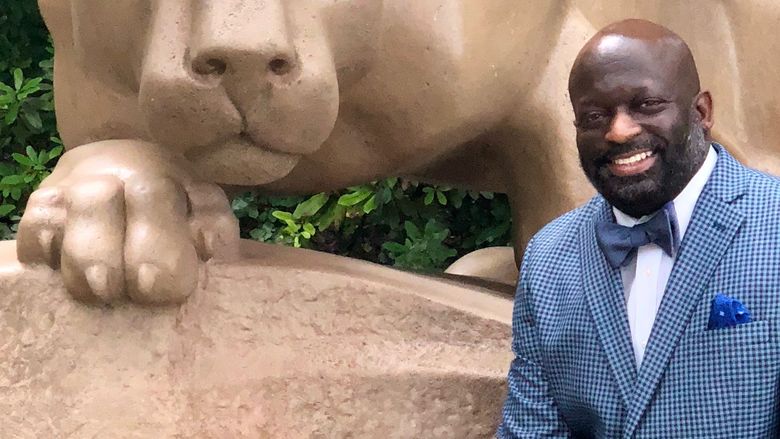 man sitting next to the Nittany lion shrine at university park 