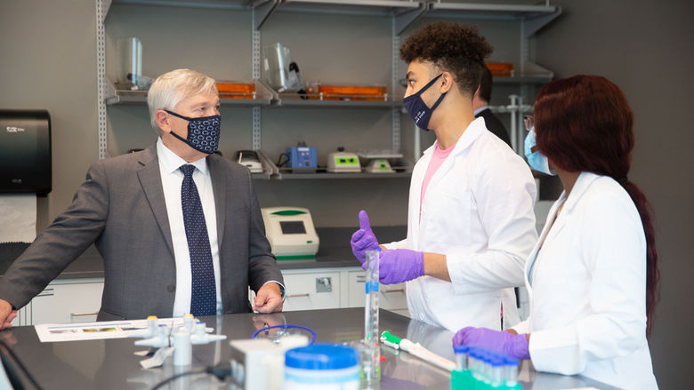 President barron looking at two students in lab coats.