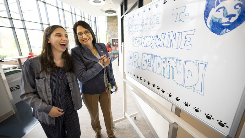 Two women stand next to a white board with a welcome message.