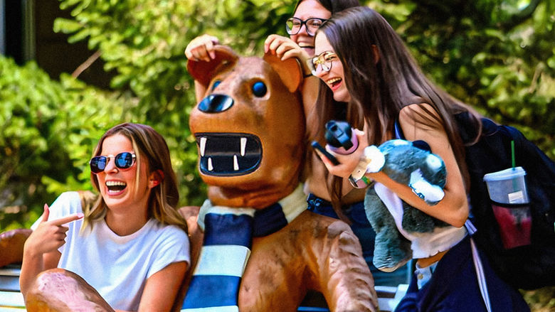 A group of female students share laughter and smiles as they pose for a photo with the iconic Nittany Lion mascot