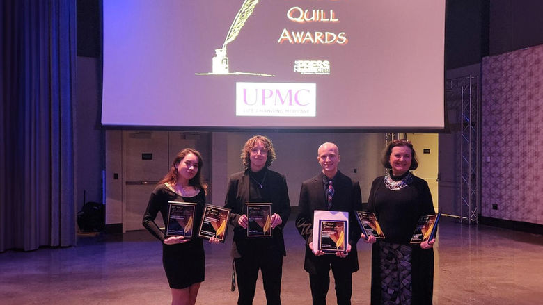 Four smiling people holding award plaques