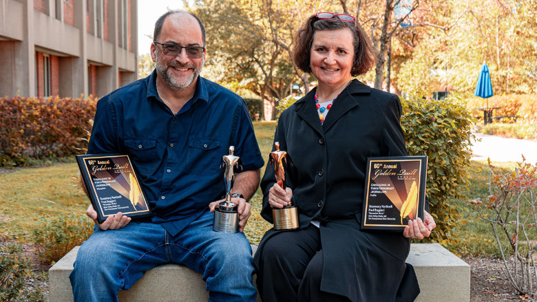 two people outside each holding a plaque and an award statute.  