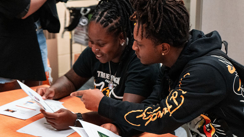 two students seated at a table reviewing a class handout