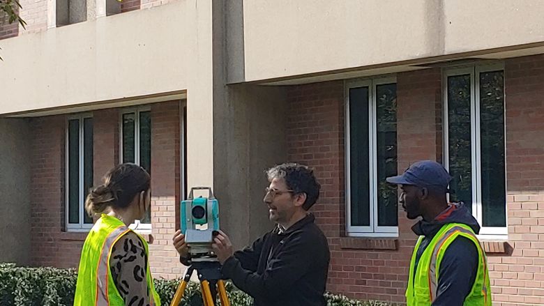 two students and a professor setting up a surveying camera in front of building