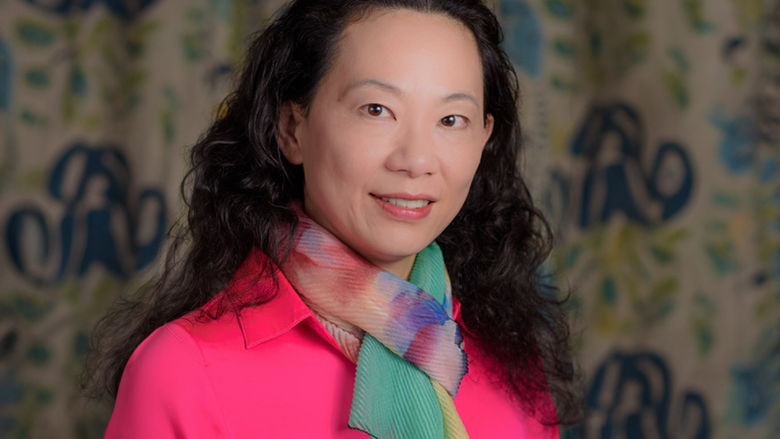 Woman wearing a pink shirt and a colorful scarf, stands in front of a patterned background