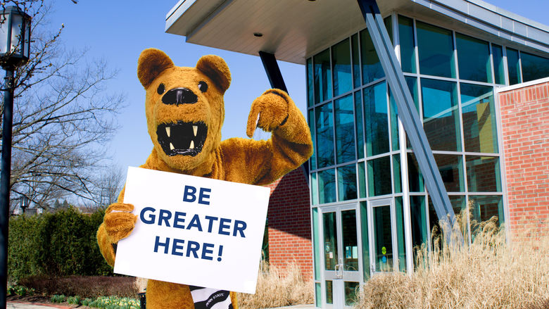 Lion mascot holding sign that says Be Greater Here. 