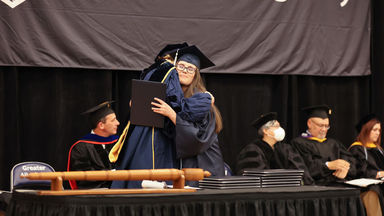 Student Marshal for Criminal Justice (B.S.), Samantha Penascino, receiving a hug and her diploma from Program Marshal for Administration of Justice and Criminal Justice, Dr. Kate McLean.