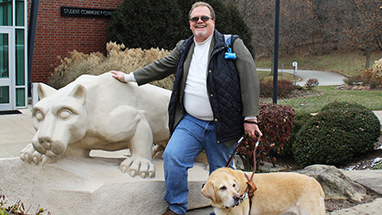 Jerry Pastories and Service Dog Nittany standing in front of the lion shrine on Greater Allegheny Campus