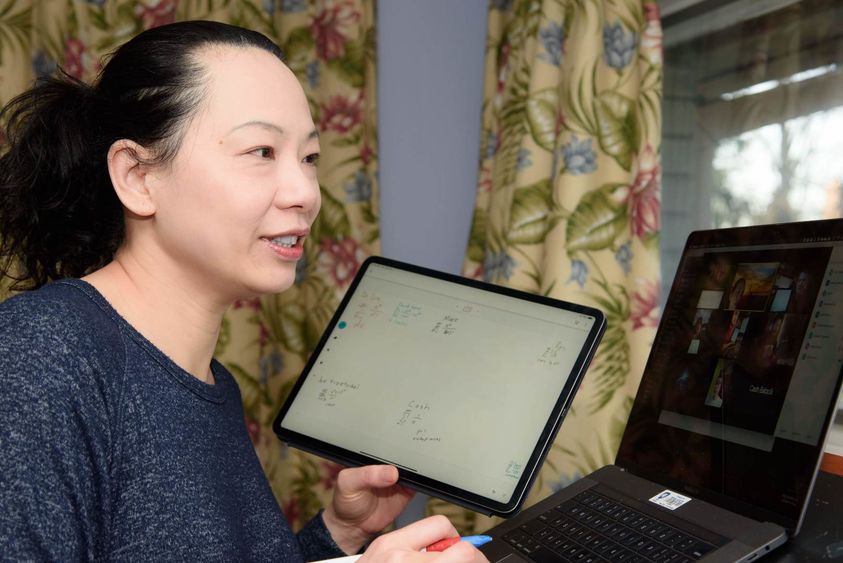 Woman holding iPad while video conferencing on a laptop with students