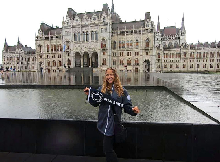 Student holding Penn State Flag in front of water feature