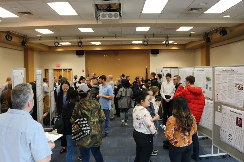 a big room with research poster on pin boards and a lot of people reviewing the research.