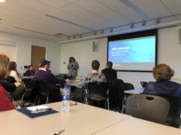 Dr. Jacqueline Edmondson standing in front of a projector screen that shows slide talking to audience members.